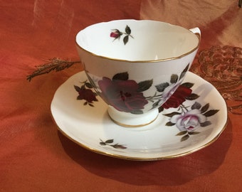 May include: A white teacup and saucer with a gold rim and a floral design featuring red and white roses.
