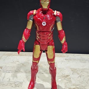 Pu&ograve; includere: Figurina di Iron Man rossa e dorata con un petto che si illumina. La figura &egrave; in piedi su una superficie bianca.