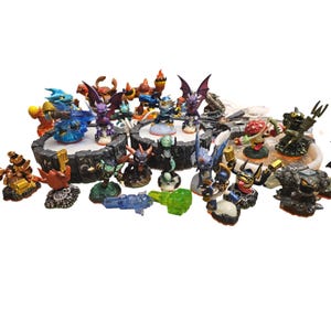 May include: A collection of colourful action figures, featuring various characters with unique designs. The figures are posed on platforms and bases, showcasing a variety of colours and textures. Some figures have wings, while others hold weapons.