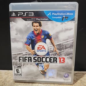 Puede incluir: Caja de juego FIFA Soccer 13 para PlayStation 3. La portada presenta a un jugador de fútbol con una camiseta azul y roja, con el logo de EA Sports. El juego es compatible con PlayStation Move.