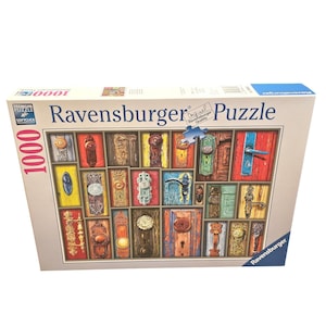 Puede incluir: Un rompecabezas Ravensburger de 1000 piezas con un collage de puertas coloridas con varios pomos y manijas. La caja del rompecabezas muestra el nombre de la marca y las palabras "Puzzle" y "Original Quality".