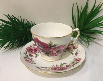 May include: A white teacup and saucer with a floral pattern. The cup and saucer have a gold trim. The flowers are pink and white with green leaves.