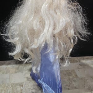 May include: A doll with long, white, wavy hair wearing a blue dress with a sparkly texture.