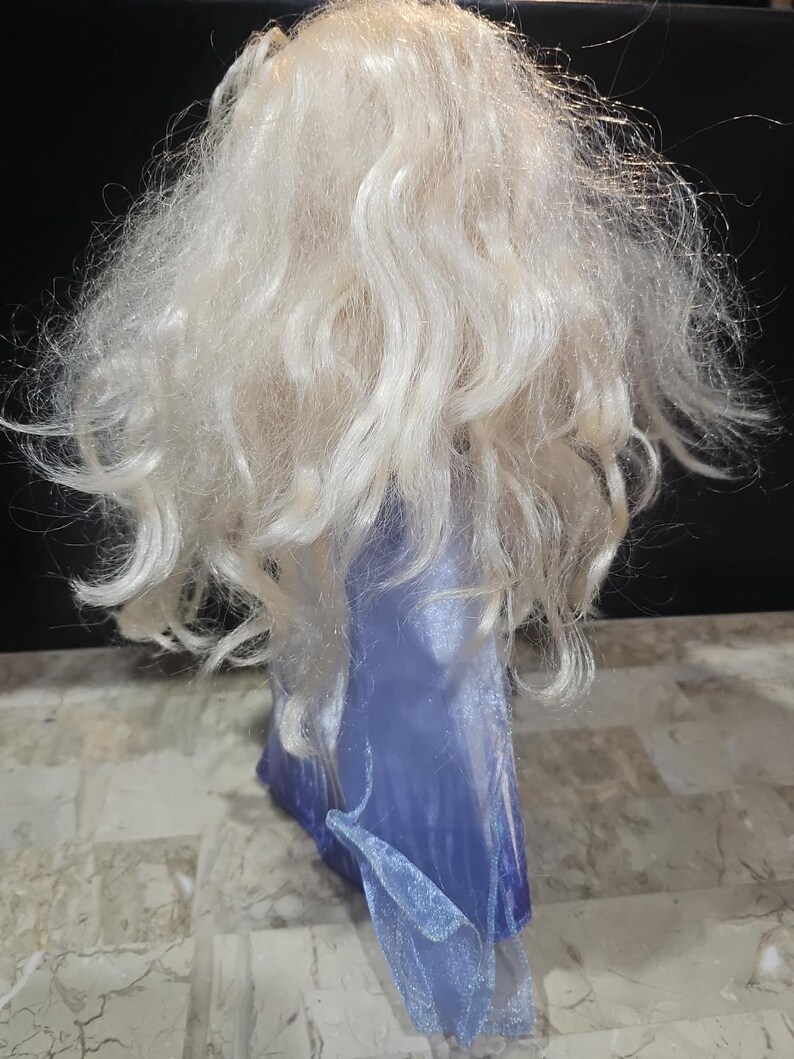 May include: A doll with long, white, wavy hair wearing a blue dress with a sparkly texture.