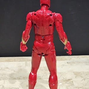 Pu&ograve; includere: Figurina di azione in plastica rossa e dorata di Iron Man, in piedi con le spalle alla telecamera. La figura ha un design dettagliato ed &egrave; in posa con le braccia ai lati.