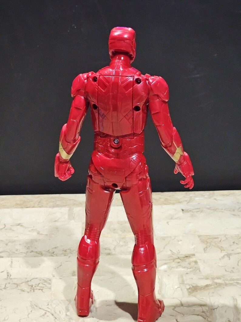 Pu&ograve; includere: Figurina di azione in plastica rossa e dorata di Iron Man, in piedi con le spalle alla telecamera. La figura ha un design dettagliato ed &egrave; in posa con le braccia ai lati.