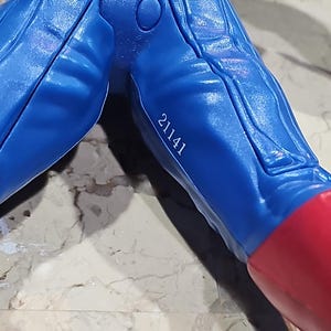 May include: Close-up of a blue plastic toy figure's lower body with a red boot and the number 21141 printed on the leg.