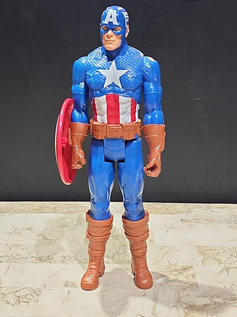 May include: A plastic action figure of Captain America, wearing his iconic red, white, and blue costume. He is holding his red, white, and blue shield in his left hand. The figure is approximately 12 inches tall.