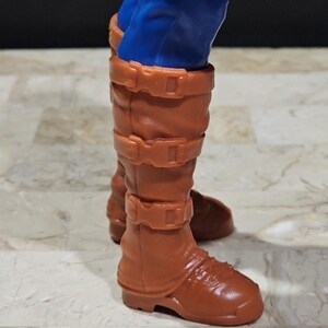 May include: Brown leather boots with buckles and a pointed toe. The boots are worn by a figure with blue pants.