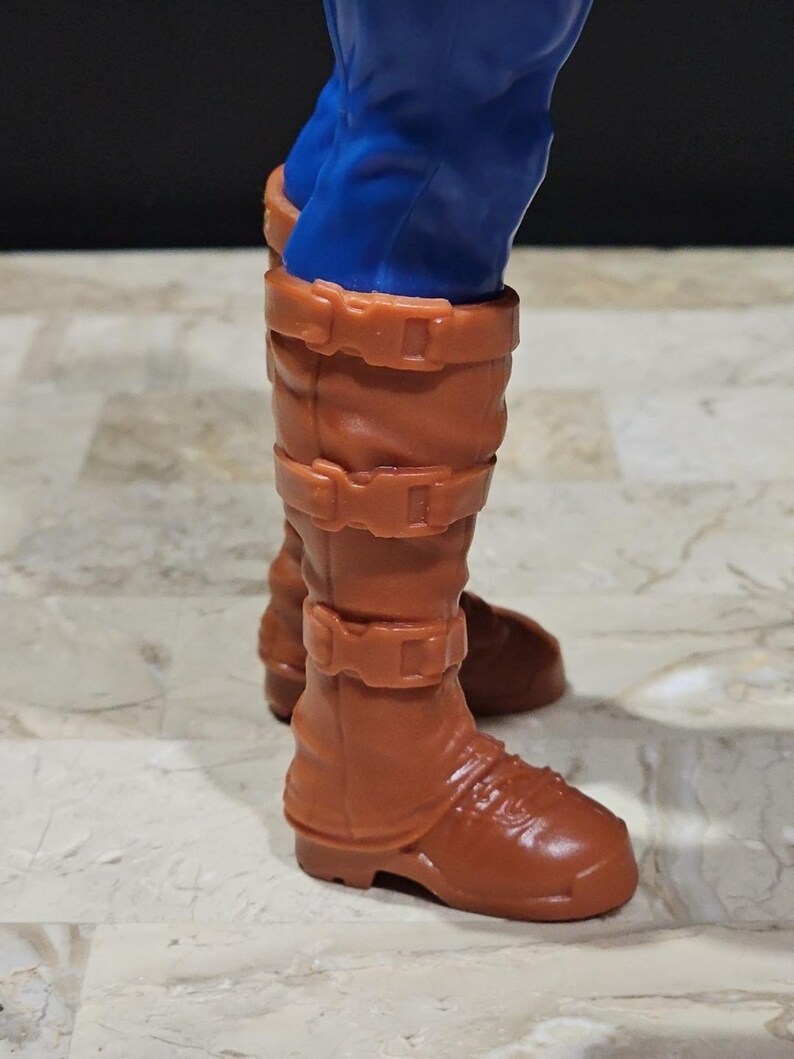 May include: Brown leather boots with buckles and a pointed toe. The boots are worn by a figure with blue pants.