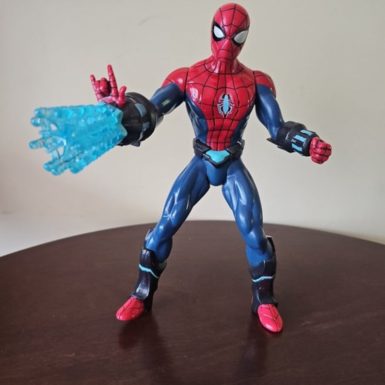 May include: Action figure of Spider-Man wearing a red and blue suit with a blue and black web shooter in his right hand. The figure is posed in a fighting stance.