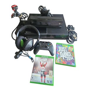 Può includere: Una console Xbox One nera con un sensore Kinect, un controller, un'auricolare e due custodie di gioco. Le custodie di gioco sono per "Just Dance 2014" e "NHL 16". L'auricolare ha cuscinetti verdi.