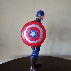 以下が含まれることがあります： 赤、白、青のキャプテンアメリカのフィギュアで、盾を持っています。フィギュアは青と赤の服を着て、赤いマントを羽織っています。フィギュアは赤、白、青の盾を持っています。