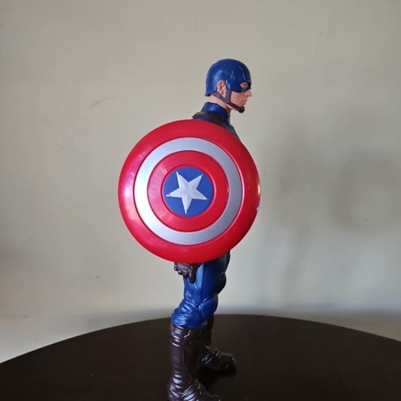 以下が含まれることがあります： 赤、白、青のキャプテンアメリカのフィギュアで、盾を持っています。フィギュアは青と赤の服を着て、赤いマントを羽織っています。フィギュアは赤、白、青の盾を持っています。