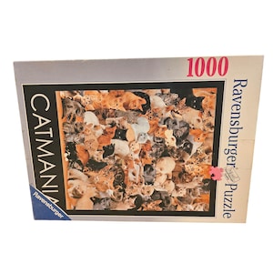 以下が含まれることがあります： 「Catmania」というタイトルのラベンスバーガー1000ピースジグソーパズル。茶色、黒、白、グレーの色合いのさまざまな猫の品種のコラージュが特徴です。パズルボックスにはラベンスバーガーのロゴがあります。