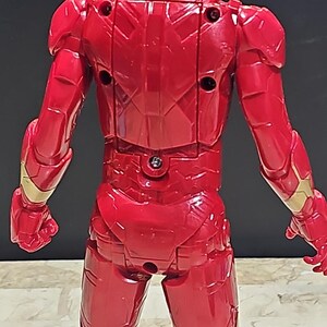 Pu&ograve; includere: Figurina di azione in plastica rossa di Iron Man, in piedi con le braccia distese, vista da dietro. La figura ha una tuta rossa dettagliata, testurizzata, con accenti dorati.