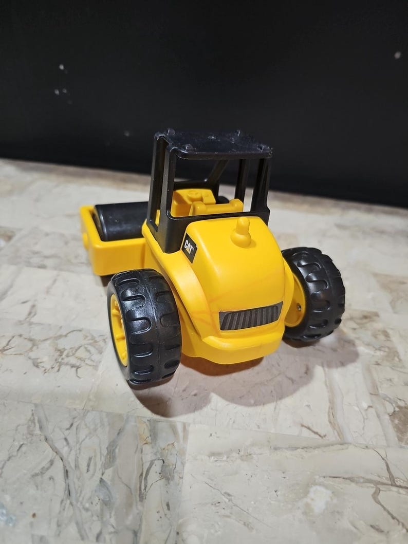 Puede incluir: Un veh&iacute;culo de construcci&oacute;n de juguete amarillo con ruedas negras y una cabina negra. El veh&iacute;culo tiene la palabra "CAT" impresa en el lateral.