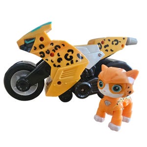 May include: A yellow and black toy motorcycle with a cheetah print design, paired with an orange and white toy cat figure. The motorcycle has black wheels and a silver accent. The cat figure is wearing an orange helmet.