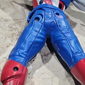 May include: A blue and red action figure of a superhero with a white star on the chest. The figure has a number 21141 printed on the leg.