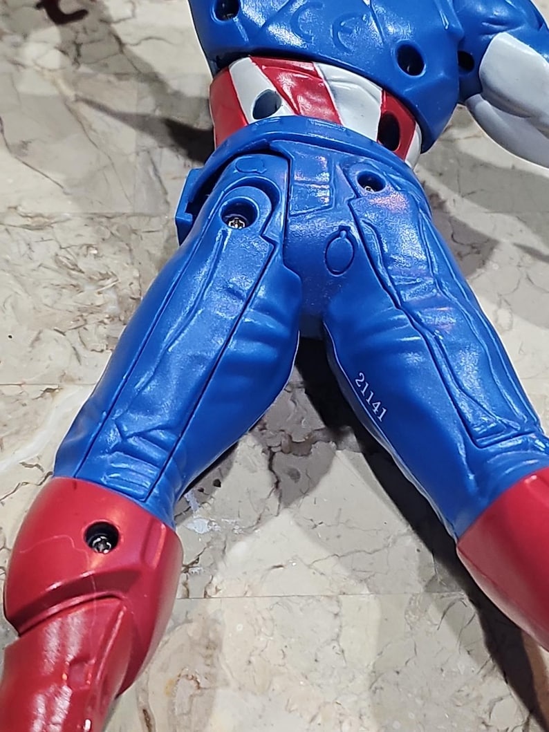 May include: A blue and red action figure of a superhero with a white star on the chest. The figure has a number 21141 printed on the leg.