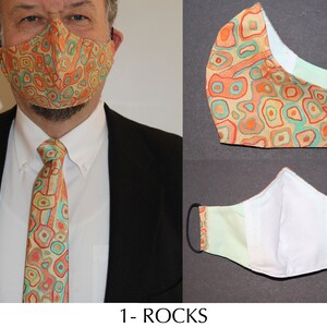 Puede incluir: Un conjunto de mascarilla y corbata con un patrón repetido de formas naranjas, turquesas y beige. La mascarilla tiene presillas elásticas negras. La corbata se lleva con una camisa blanca y una blazer negra. El texto "1- ROCKS" está en la parte inferior.