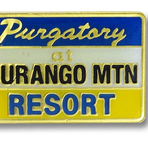May include: A gold-colored metal pin with a blue, white, and yellow design. The pin reads "Purgatory at DURANGO MTN RESORT".