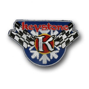 May include: Embroidered patch with a blue background, the word "keystone" in red, and a white "K" inside a red and yellow circle. Features checkered flags and snowflake designs.