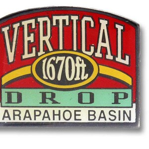 May include: A red, yellow, and green sign with the text "VERTICAL 1670ft DROP ARAPAHOE BASIN".