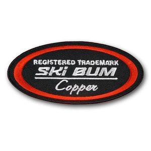 May include: Black oval patch with red stitching around the edge. The text "REGISTERED TRADEMARK" is above the text "SKI BUM" in white. The text "Copper" is below "SKI BUM" in white cursive.