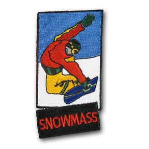 Puede incluir: Parche bordado con un snowboarder con ropa roja, amarilla y azul, realizando un truco sobre un fondo de cielo azul. El parche tiene la palabra "SNOWMASS" en letras rojas sobre un fondo negro.