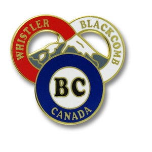 May include: A gold-colored pin with a red, white, and blue design. The pin features a stylized mountain with the words "Whistler" and "Blackcomb" on the top and "BC Canada" on the bottom.