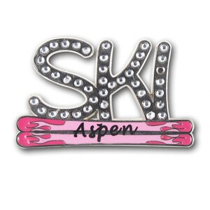 May include: A silver pin with the word "SKI" in rhinestones, with a pink and red ski design underneath that says "Aspen".