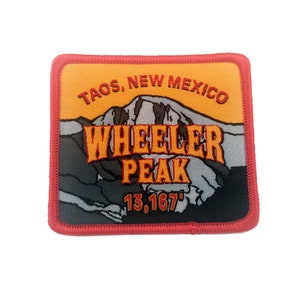 Może przedstawiać: Naszywka haftowana w kolorze czerwonym, białym i pomarańczowym z tekstem "Taos, Nowy Meksyk" i "Wheeler Peak 13,167'" na żółtym tle. Naszywka przedstawia scenę górską z szarym szczytem.