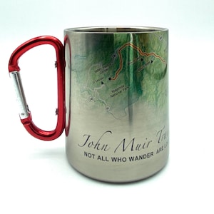 May include: Stainless steel travel mug with a red carabiner handle. The mug features a map of the John Muir Trail with the text "John Muir Trail" and "Not all who wander are lost".