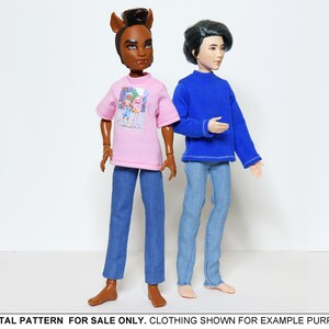 May include: Two dolls wearing casual clothing. One doll is wearing a pink t-shirt with a graphic print and blue jeans. The other doll is wearing a blue long-sleeved shirt and blue jeans.