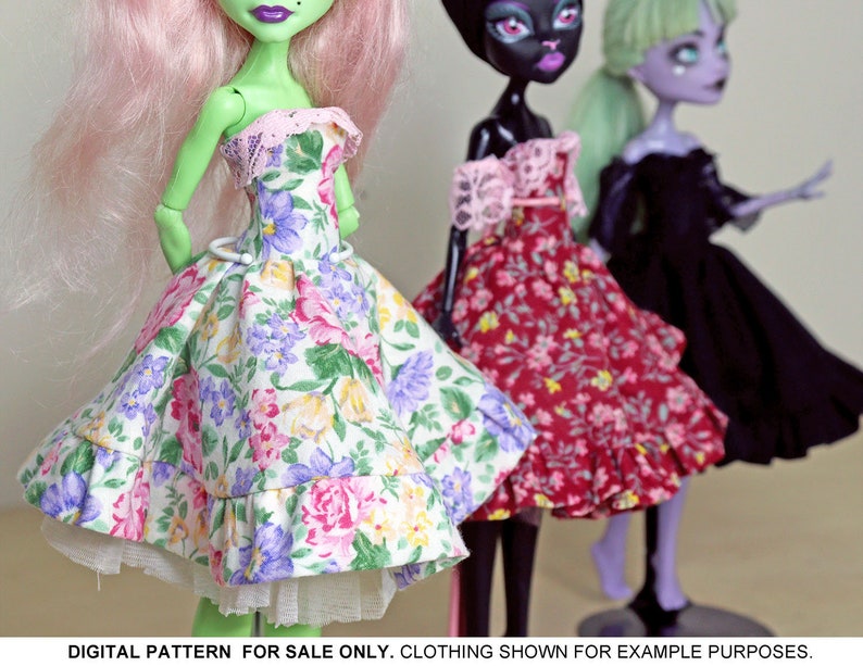 May include: Three dolls wearing floral print dresses. The doll on the left is green with pink hair and is wearing a white and green floral dress with a white lace trim. The doll in the middle is black with black hair and is wearing a red and white floral dress with a pink lace trim. The doll on the right is purple with green hair and is wearing a black dress.