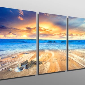 May include: A three-panel canvas print depicting a seascape with a golden sunset over the ocean. The waves are crashing on the sandy shore, creating a sense of tranquility and beauty.
