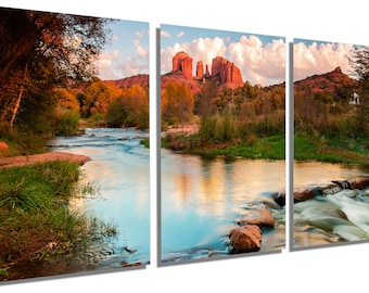 May include: A scenic landscape photograph of a river flowing through a woodland with red rock formations in the background. The river is calm and reflects the sky and clouds. The trees are green and yellow, indicating autumn.