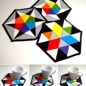 Könnte beinhalten: Drei sechseckige Stoffuntersetzer mit einem geometrischen Sternmuster in leuchtenden Farben wie Rot, Orange, Gelb, Grün, Blau und Violett, kontrastiert durch schwarze, weiße und graue dreieckige Segmente, jeweils mit einem schwarzen Stoffrand.