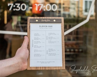 May include: A wooden clipboard with a dark metal top clip holding a white menu titled SLOVEN BAR. The menu lists various craft beers, cocktails, and mocktails with prices. The wood has a visible grain pattern and the metal clip features the text Shopdaddy-Studio.