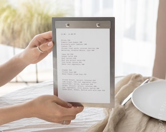 May include: A rectangular metal menu holder with a silver finish and two circular fasteners at the top, securing a white paper menu printed with black text listing various food items and prices, held upright in a vertical orientation.