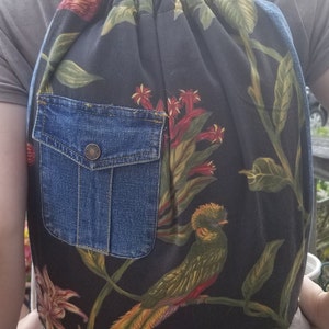 Peut inclure: Un sac à dos noir à cordon avec un imprimé floral représentant des oiseaux et des feuilles. Le sac à dos a une grande poche en jean à l'avant.
