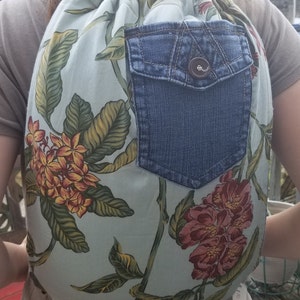 May include: A light blue drawstring backpack with a floral print. The backpack has a large denim pocket on the front with a button closure.