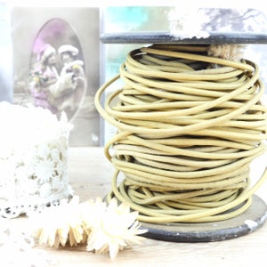 May include: A spool of beige cord or rope wound tightly on a wooden base. The cord is smooth and has a slight sheen. The spool is sitting on a wooden surface.