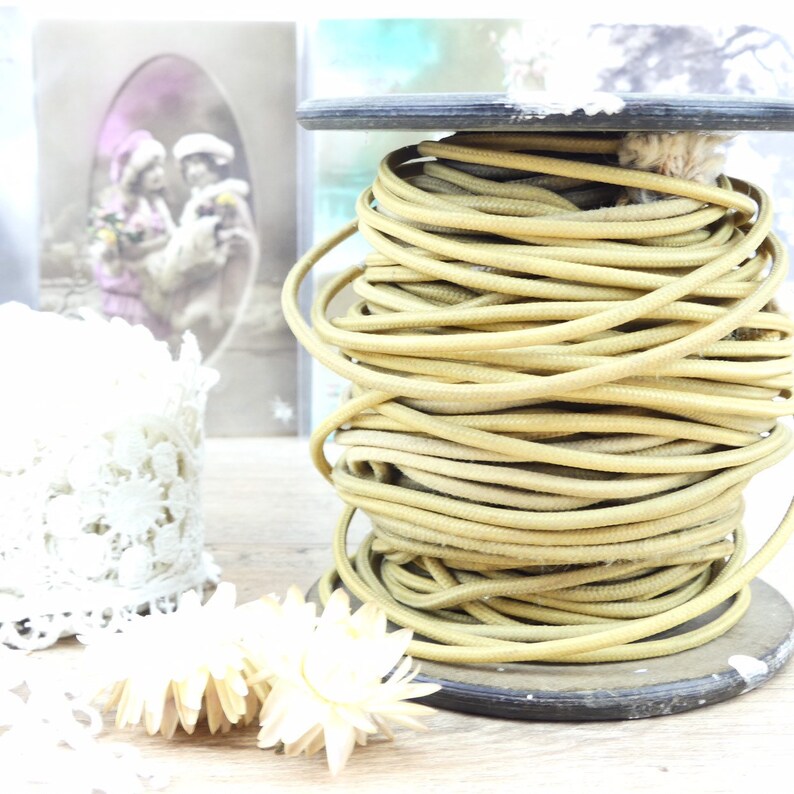 May include: A spool of beige cord or rope wound tightly on a wooden base. The cord is smooth and has a slight sheen. The spool is sitting on a wooden surface.