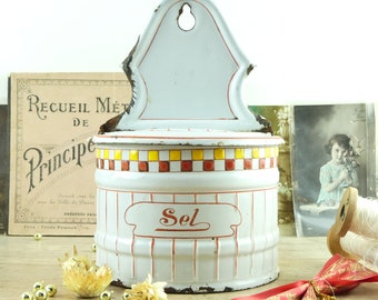 May include: White enamel wall mounted salt container with red and yellow checkered trim and the word "Sel" in red lettering.