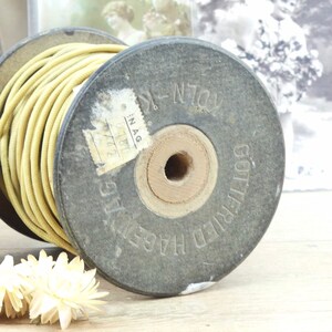 May include: A spool of yellow electrical wire wrapped around a wooden and black painted spool. The spool is labeled "Gottfried Hage" and "IN.AG 1870 742".