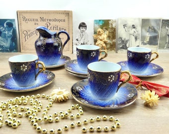May include: A set of four blue and gold teacups and saucers with a white interior. The cups and saucers have a floral design with gold accents. There is also a matching blue and gold creamer.