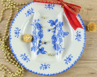 May include: A white ceramic serving dish with a blue and white floral pattern. The dish has two sections and is decorated with gold accents. A red ribbon with music notes is tied around the dish.