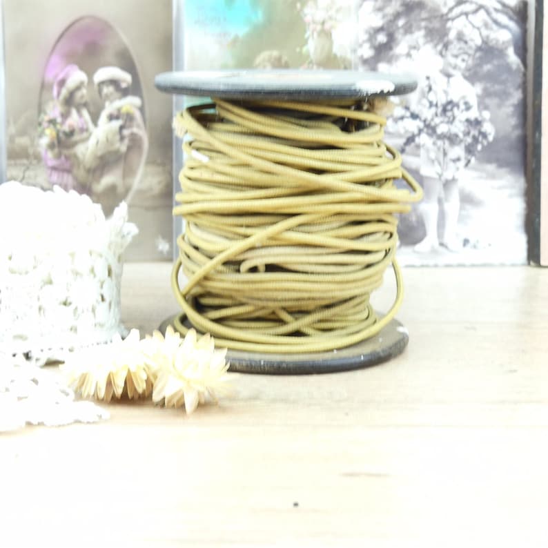May include: A spool of gold-colored cord or wire on a wooden spool. The spool is sitting on a wooden surface.